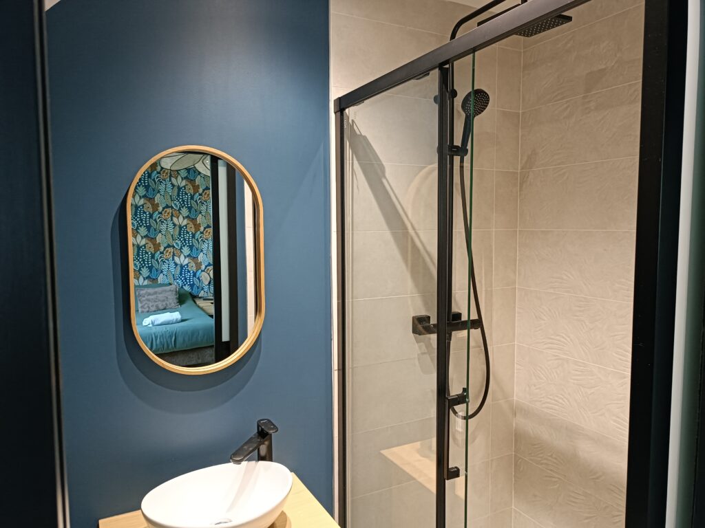Salle d’eau privative de La Vintage avec meuble vasque en bois, miroir rond et douche